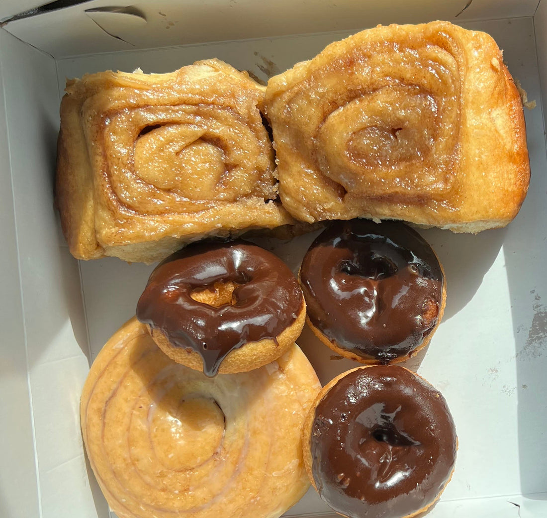 box of baked goods with caramel rolls and donuts iced with chocolate. Photo taken by author.